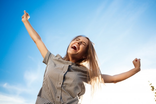 Frau steht mit in den Himmel gestreckten Armen da und freut sich vor sonnigem Hintergrund, happiness coach, frankfurt